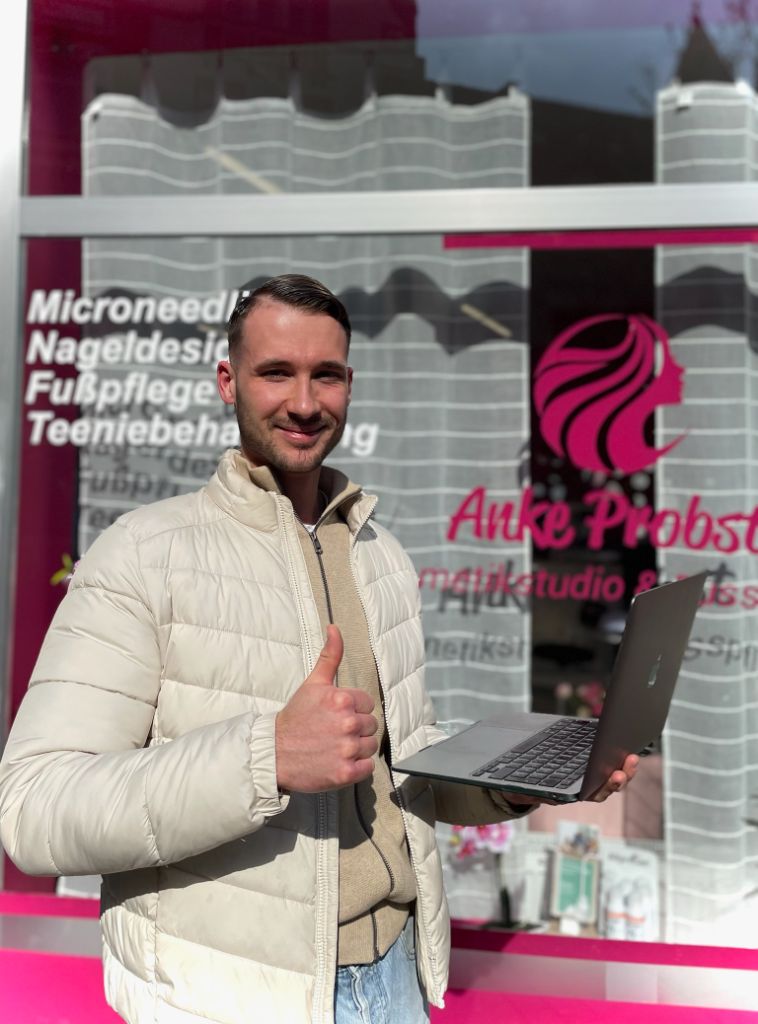 Dean Aaron Budde vor dem Schaufenster von Anke Probst Kosmetikstudio & Fußpflege mit Laptop